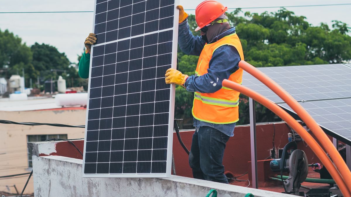 A solar technician carrying a solar panel to be installed