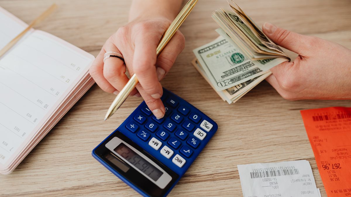 A person using a calculator next to money and receipts to work out savings